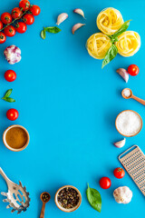 Frame of ingredients for cooking Italian pasta - uncooked fettuccine with tomatoes and basil leaves - on a blue background, top view