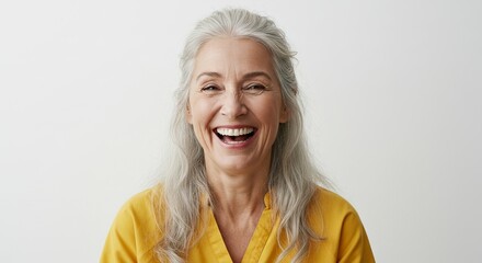 A smiling older woman with gray hair wearing a yellow shirt against a plain white background