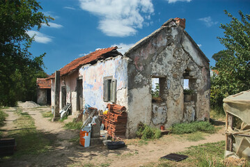Abandoned deteriorating rural house with red tile roof and weathered walls in Serbian countryside village