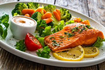 Fried salmon steak with boiled broccoli and mini carrots and mayonnaise on wooden table	