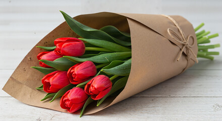 Wrapped bouquet of red tulips with green leaves tied with twine on rustic wooden background