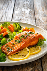 Fried salmon steak with boiled broccoli and mini carrots and mayonnaise on wooden table	