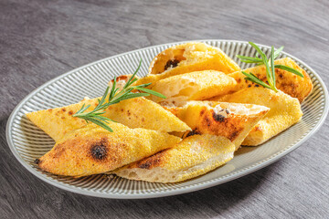 Crispy focaccia bread pieces sprinkled with cornmeal and garnished with fresh rosemary on a ceramic plate