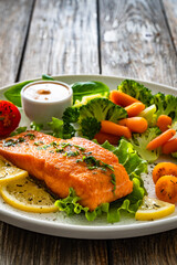 Fried salmon steak with boiled broccoli and mini carrots and mayonnaise on wooden table	