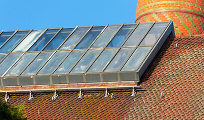 glass roof structure with skylight panels on an old tiled industrial building and a red brick chimney in sunlight