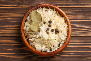 Bowl with tasty sauerkraut, peppercorns and bay leaves on wooden background