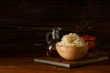 Bowl with tasty sauerkraut, peppercorns and bay leaves on wooden background