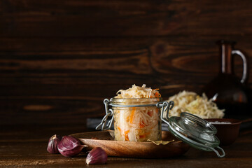 Jar with tasty sauerkraut and garlic on wooden background