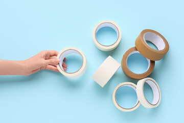 Female hand with rolls of different masking tape on blue background
