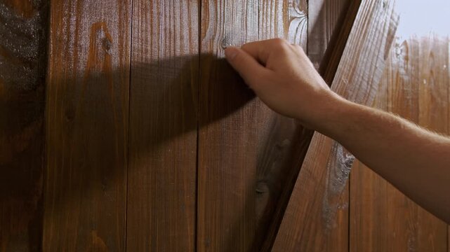 A closeup view of a hand gently knocking on a rustic wooden door, emphasizing the intricate textures and shadows
