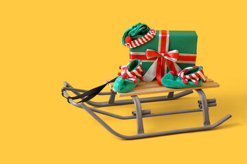 Sled with Christmas gift and festive clothes on yellow background
