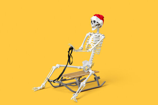 Funny skeleton in Christmas hat riding sled on yellow background