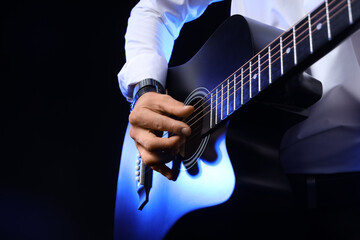 Young man playing guitar on black background