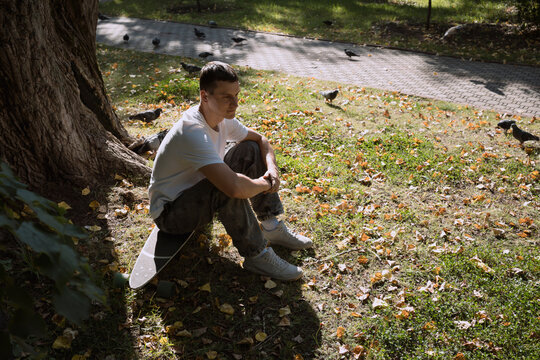 Adult man sitting on skateboarder in city park in summer day