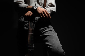 Young man with guitar on black background