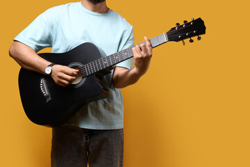 Obraz premium Young man playing acoustic guitar on yellow background