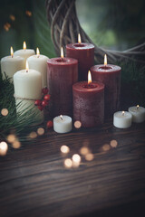 Atmospheric still life with golden bokeh. Red and white candles with natural decorations on dark wooden table. Vertical tranquil  background for quiet remembrance and mourning with space for text.