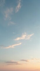 Evening sky shows light blue color blending to warm pastel pink, orange hues at horizon. Soft scattered clouds drift gently. Calm weather conditions create beautiful natural light gradient background