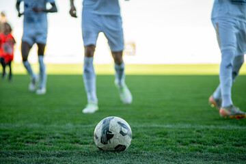 Close-up of a football on green grass with blurred players in the background, symbolizing teamwork, competition, and the spirit of the game.