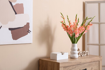 Box and vase with bouquet of beautiful gladiolus flowers on chest of drawers in living room, closeup