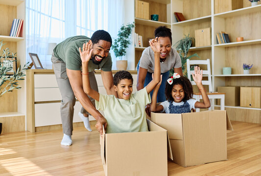 Famili of four, Father and mother  pushing their son and  daughter sitting in a cardboard box, having fun at home. Relocation, new home, family concept