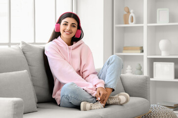 Obraz premium Beautiful young woman in modern headphones listening to music on sofa at home