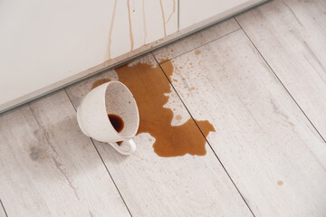 Overturned cup and spilled coffee on floor in kitchen