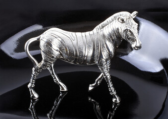 Silver zebra figurine standing on reflective black surface