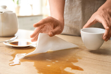 Woman with paper towel wiping coffee stains from table in kitchen