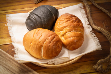 Three round croissants, one dark charcoal and two classic golden in wood plate on wooden table background, Round croissants or Croissant Buns in wood plate.