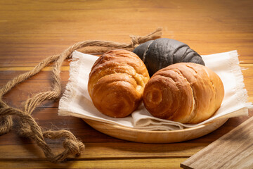 Three round croissants, one dark charcoal and two classic golden in wood plate on wooden table background, Round croissants or Croissant Buns in wood plate.