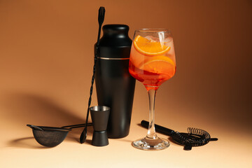 Glass of Aperol spritz cocktail and bartender tools on beige background