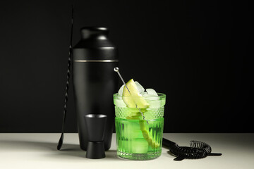Glass of fresh cocktail and bartender tools on white table near black wall, closeup
