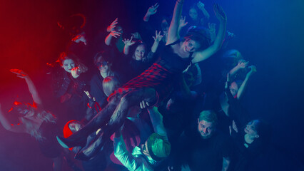 Woman crowd surfing above cheering Halloween party audience. Concept of entertainment, emotions,...