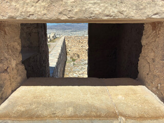 View through ancient stone blocks framing the Athens city landscape, combining historic ruins with modern skyline under sunny blue skies.