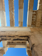 Upward view of Parthenon columns against blue sky and bright sun in Athens, showcasing classical Greek architecture and marble textures.