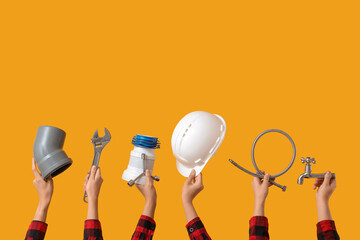 Hands with hardhat and construction tools on yellow background