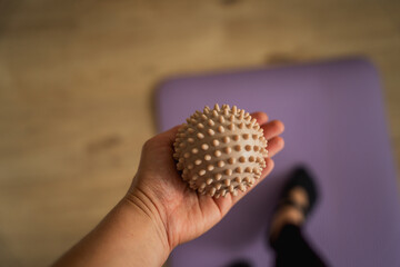 Closeup of a woman's hand holding a massage ball over a yoga mat. Home sport. Health.