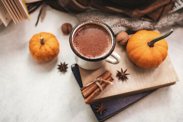 Cozy autumn still life with enamel mug of hot chocolate, pumpkins, vintage books, walnuts, cinnamon sticks, star anise and warm fall clothing, seasonal composition