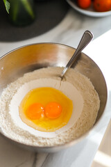 Baking ingredients: eggs and flour in mixing bowl on marble countertop