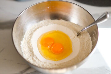 Eggs cracked in flour bowl: baking ingredients in stainless steel mixing bowl with spoon