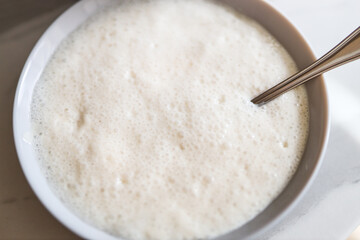 Bowl of frothy oatmeal with spoon on white surface