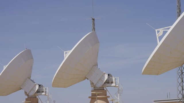 Large parabolic satellite dishes at a telecommunications ground station point to the clear blue sky. A symbol of global communication, data transmission, and modern technology.