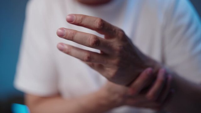 Close-up of man feeling hand discomfort, rubbing and massaging wrist and fingers, performing warm-up exercises to alleviate pain, carpal tunnel syndrome, arthritis, or cramp symptoms, slow motion.