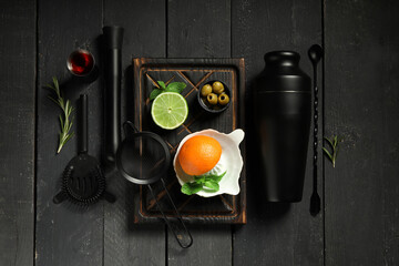 Modern bartender tools and cocktail ingredients on black wooden background