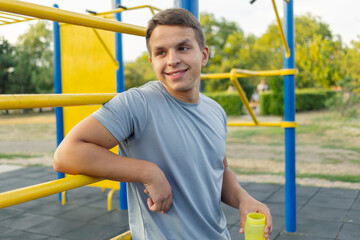 Fototapeta premium A young man standing on an outdoor sports ground drinking water after a workout