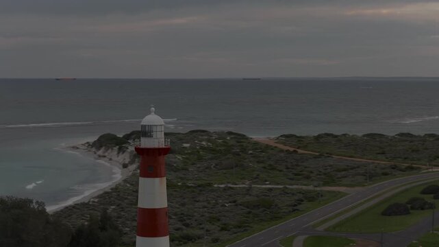 Circling aerial shot starting close to the lighthouse and then flying further back to reveal the entire lighthouse. Background starts with the port, finishing towards the sunrise.