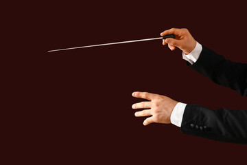 Hands of male conductor with baton on brown background