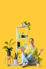 Beautiful young woman reading book near bookshelf on yellow background