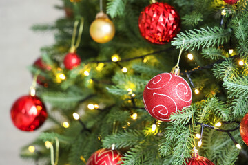 Closeup view of beautiful baubles and glowing lights hanging on Christmas tree in festive room
